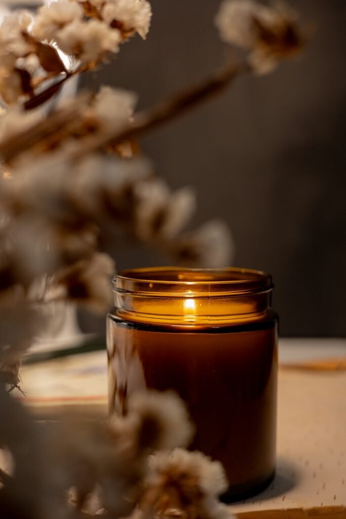 9 Best Scented Candles for Diwali 2026: Premium Gifts and Decor Amber glass jar candle glowing next to dried flowers