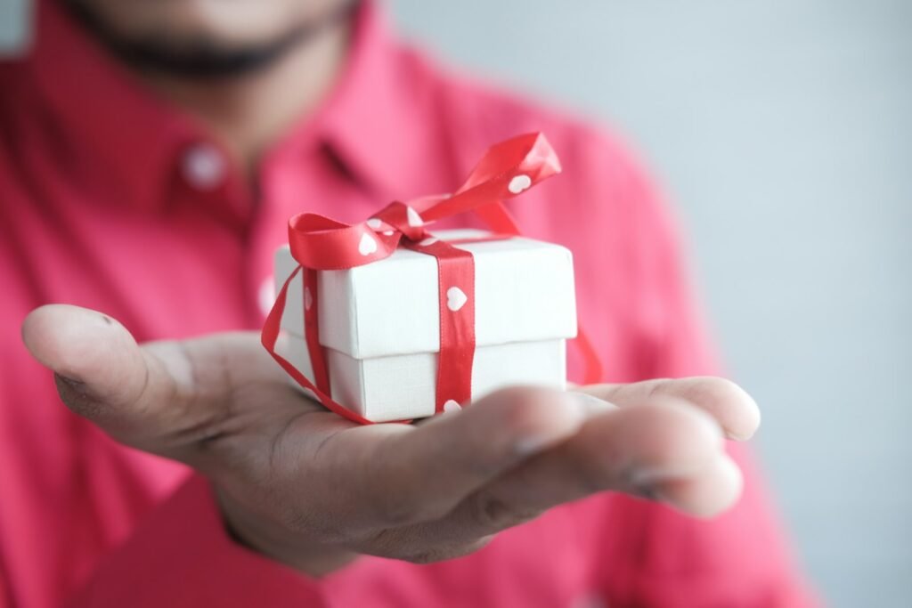 Man holding out a white gift box tied with a red ribbon