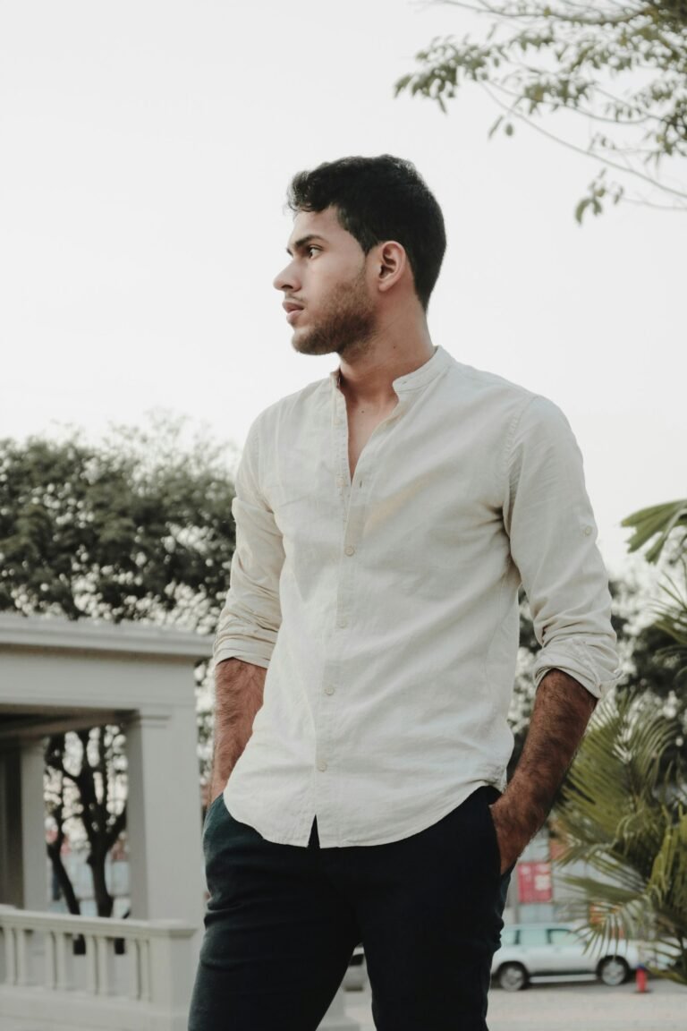 A man in a relaxed white shirt standing near green plants