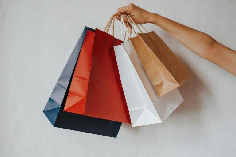 A hand holding colourful shopping bags against a white background